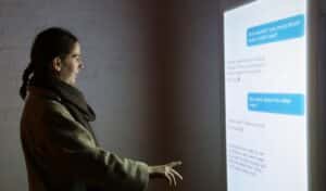 A woman stands at a large screen that is displaying text messages.